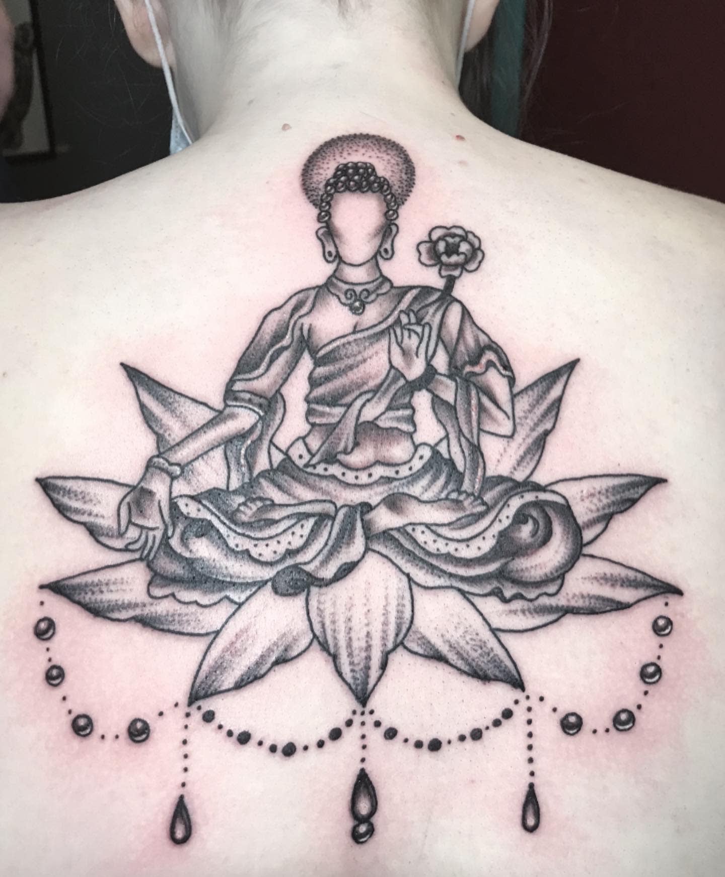 Back tattoo of a seated Buddha on a lotus flower with delicate dotwork and beads